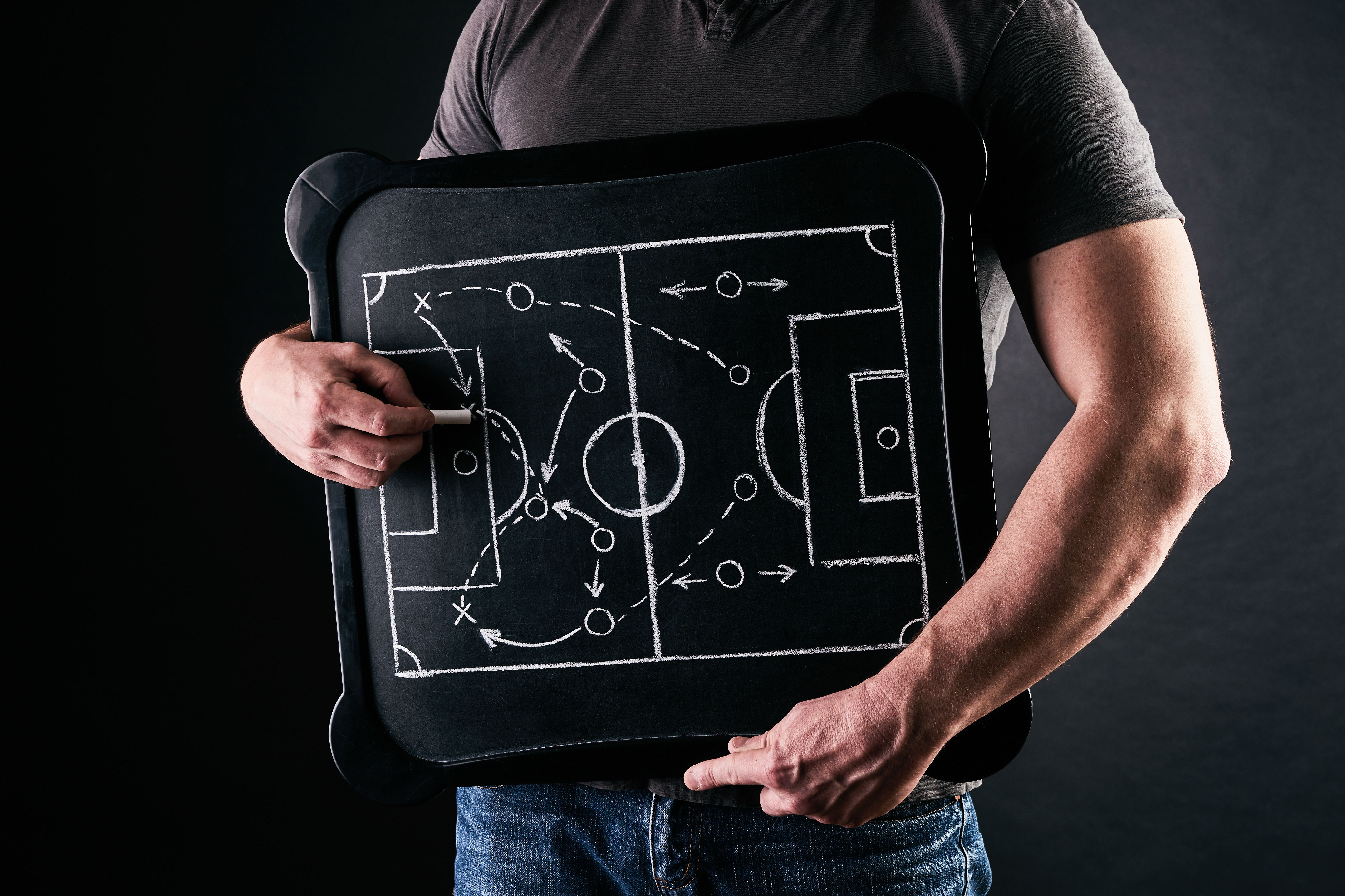 Coach's hand drawing tactical formations with chalk on a blackboard during a match time-out